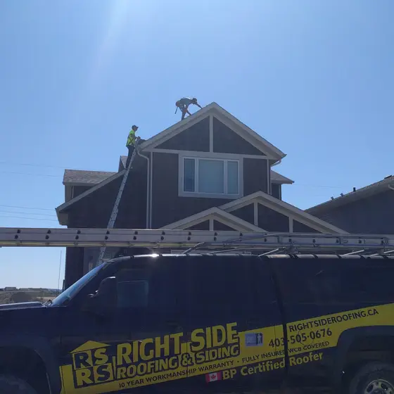 Truck at the curb with the ladder up against the eave and two roofers working on the ridge above