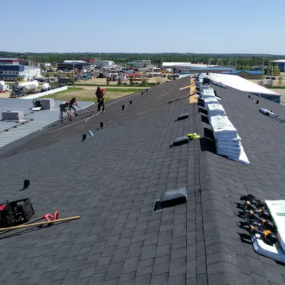 Crew re-shingling a long commercial roof, bundles and underlayment staged the length of the ridge