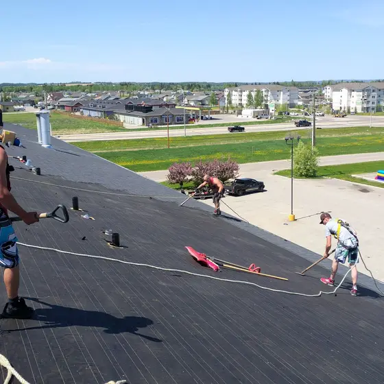 Installers in harnesses clearing a stripped low-slope roof before the new system goes down