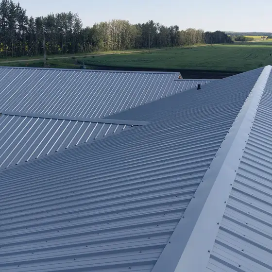 Silver standing-seam metal roof on an acreage shop, low sun across the field behind it